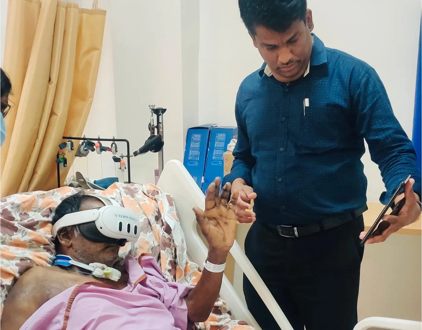 A patient in a hospital bed using a Rewin VR headset while a team member guides the session