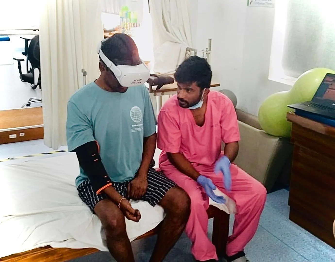 A patient wearing a Rewin VR headset and arm sensor while a therapist guides the session